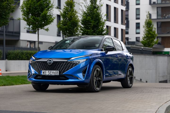 Niebieski Nissan Qashqai stojący przed budynkiem, z drzewami w tle