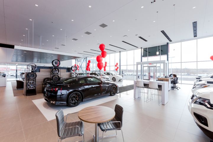 Intérieur moderne de la salle d'exposition du concessionnaire automobile avec de nouvelles voitures exposées, des ballons rouges pour la décoration et un coin salon avec tables et chaises.