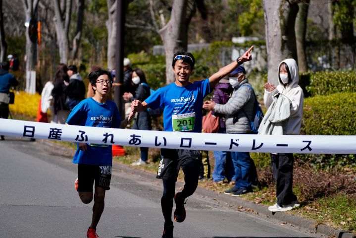 青いTシャツを身に着けた男性の選手と同じく青いTシャツを身に着けた伴走者が笑顔でゴールする様子
