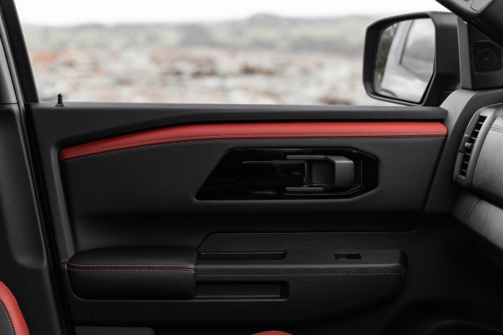 2026 Nissan Navara PRO-4X finished in Boulder Grey presenting the front passenger door panel with red stitched accent strip, gloss-black handle surround and side mirror.