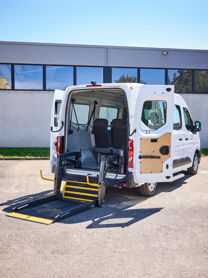 3/4 Heckansicht eines weißen Nissan Interstar-e mit MobiTEC Ausbau mit ausgeklapptem Rollstuhllift mit zwei seitlichen, gelben Haltegriffen
