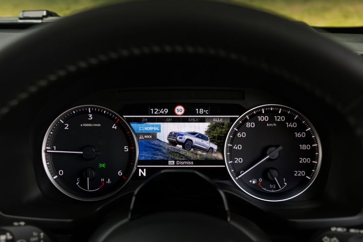 2026 Nissan Navara PRO-4X finished in Boulder Grey featuring the cluster screen with ROCK mode, hillside vehicle illustration and top drivetrain band.