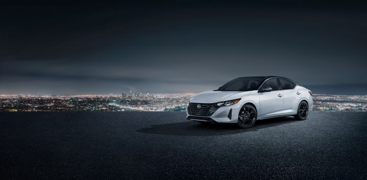 Front left 3/4 angle of a white Sentra Midnight Edition parked on a cliff that overlooks a cityscape at nighttime.