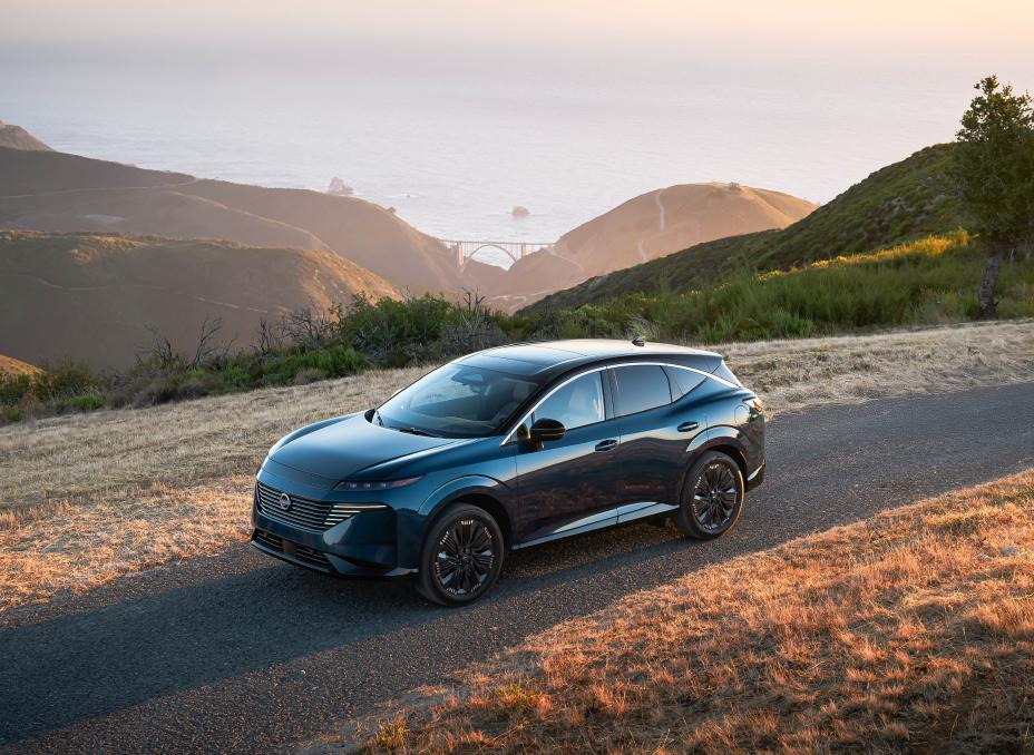 Un Nissan Murano 2025 bleu foncé roulant sur une route pavée à haute altitude avec des collines ondulantes et un grand plan d’eau en arrière-plan