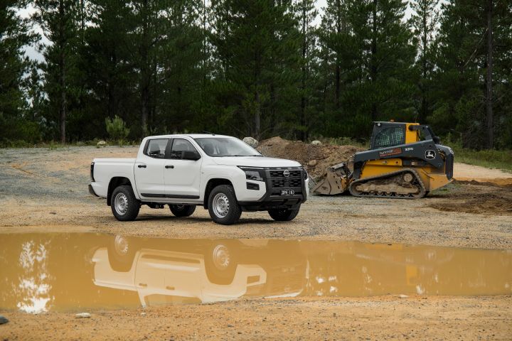 2026 Nissan Navara SL dual cab ute finished in Alpine White photographed on a gravel worksite beside muddy water, with a compact loader visible in the background.