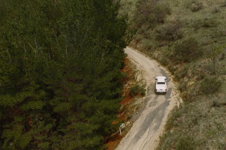 Distant shot of an Alpine white Nissan Navara driving up a dirt road bend