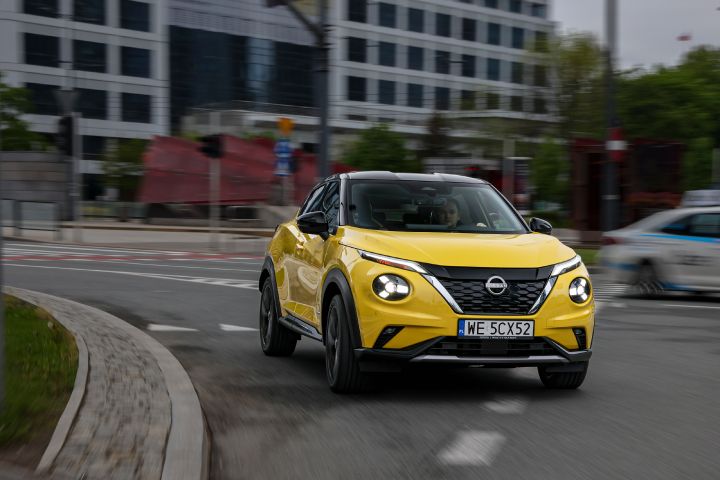 Jadący żółty Nissan Juke (widok z przodu) z budynkami w tle
