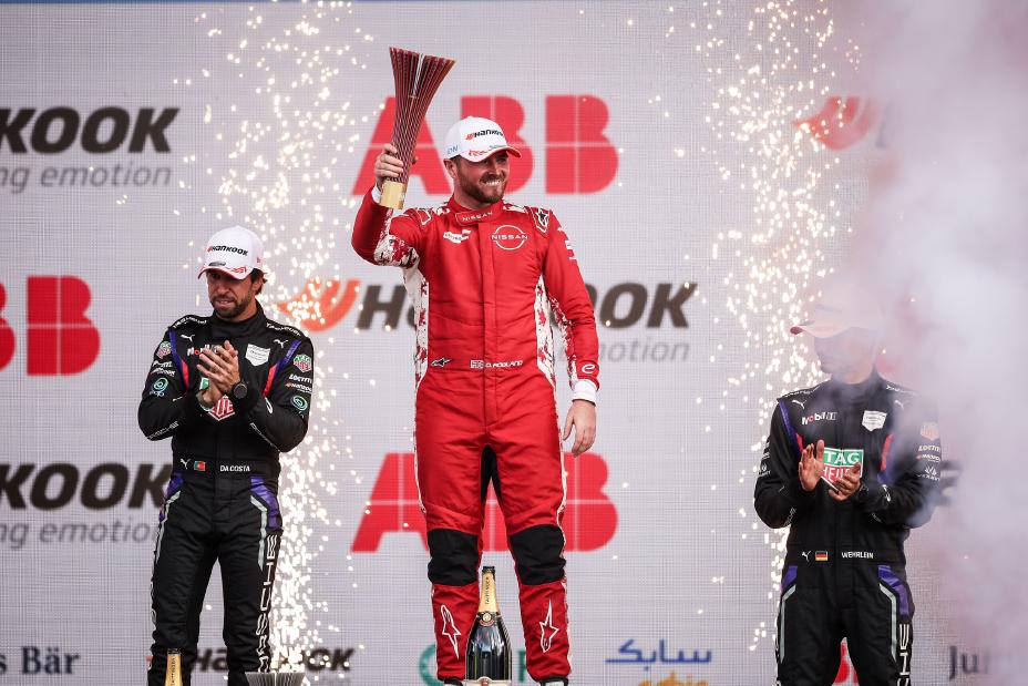 Oliver Rowland pozdrawia tłum ze swoim trofeum na najwyższym stopniu podium.