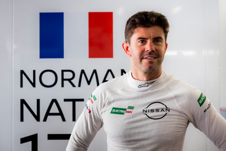 Norman Nato lächelt in der Teamgarage mit seinem weißen, feuerfesten Nissan Rennanzug.