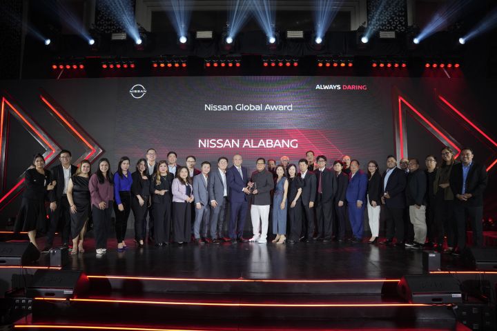 Group of awardees and executives on stage receiving the Nissan Global Award for Nissan Alabang, with a trophy presentation and red-lit event backdrop displaying Nissan branding and “Always Daring.”