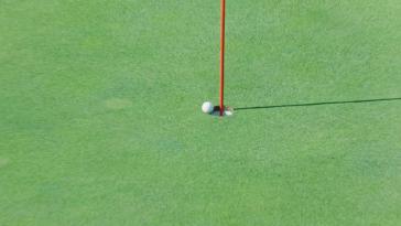 An image of a golf ball teetering on the edge of a hole