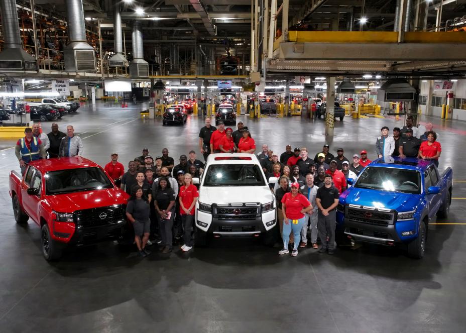 Three Nissan trucks parked on a warehouse floor with employees standing nearby for a picture.
