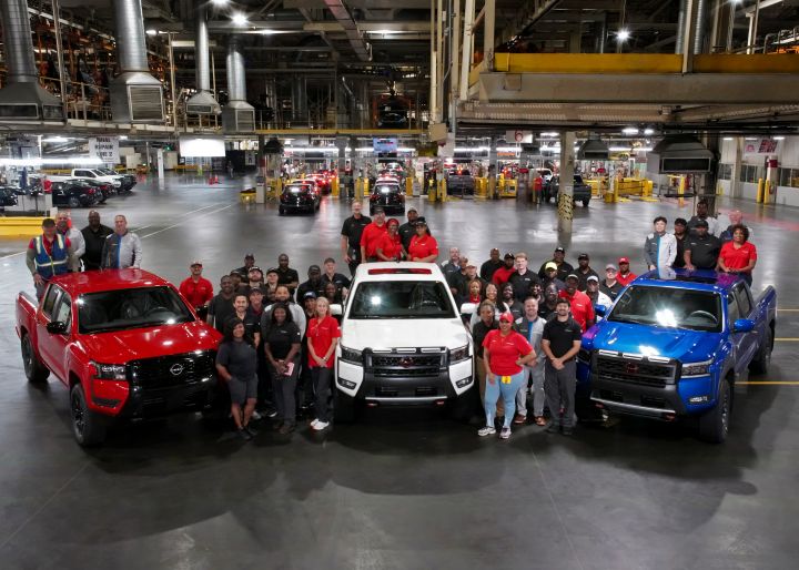Three Nissan trucks parked on a warehouse floor with employees standing nearby for a picture.