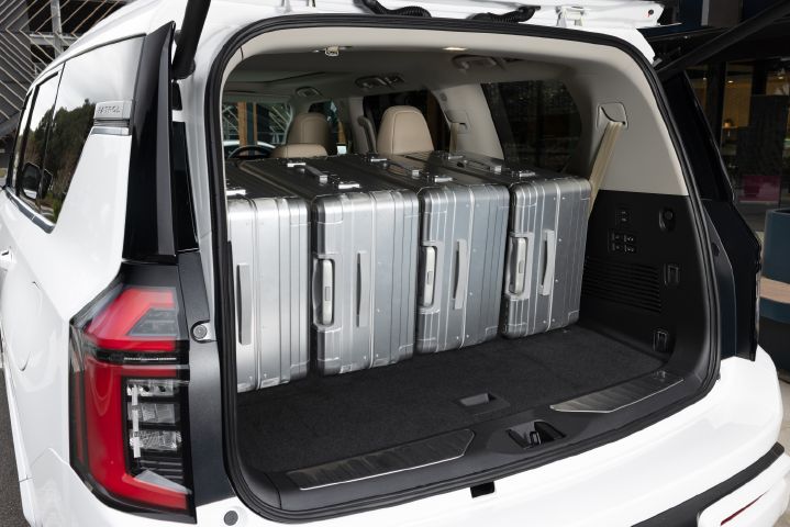 2026 Nissan Y63 Patrol finished in white, rear cargo area shown with the tailgate open, third-row seats folded flat and four large silver suitcases loaded inside.