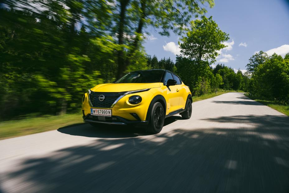 Gelber Nissan Juke von schräg vorne fährt auf einer Landstraße, im Hintergrund stehen grüne Bäume