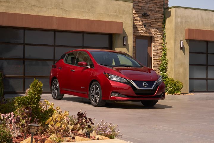 A red Nissan LEAF parked in the driveway of a luxury home