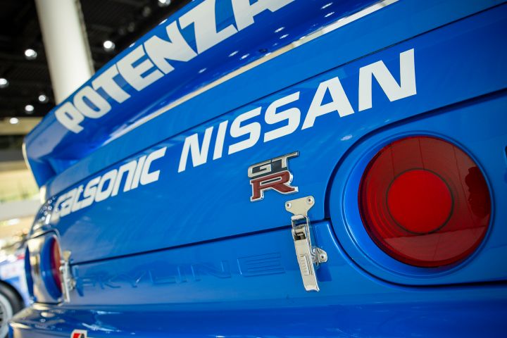 A close up view of the rear tail lamp and trunk lid of a blue GT‑R race car with "Calsonic Nissan" wording across rear.