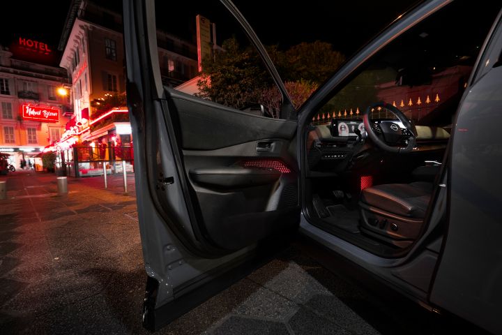 Vue de l'intérieur d'une Nissan Ariya NISMO avec des matériaux noirs, en arrière-plan une rue nocturne avec des enseignes lumineuses