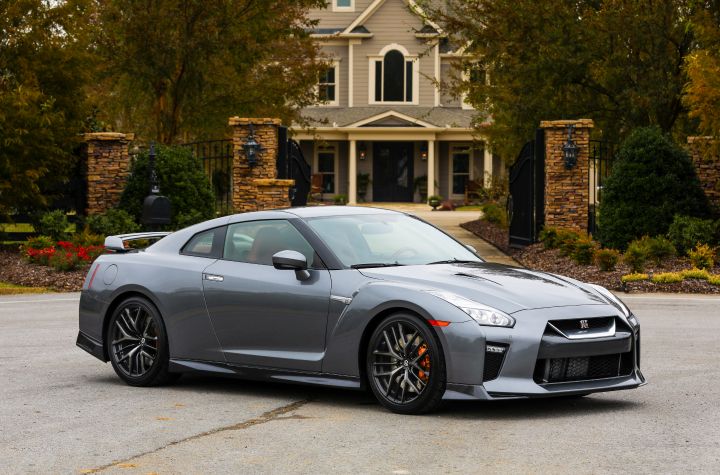 A gray Nissan GT‑R parked in front of a house with a stone entrance and autumn trees.
