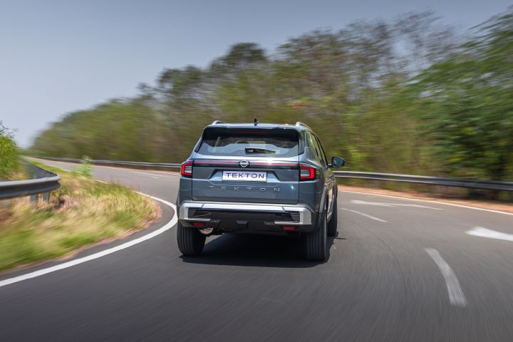 Rear view of the Nissan Tekton rounding a curve on a forested road.