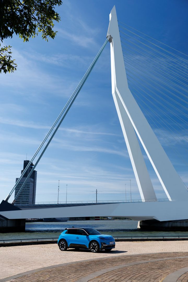 Bild einer großen Brücke in Rotterdam mit hohem weißen Pfeiler, davor steht in der Sonne ein blauer Nissan Micra