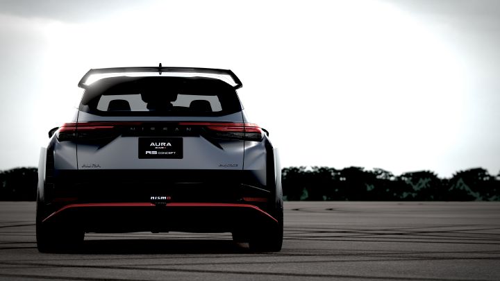 A silver and black two-tone sports car, the Aura Nismo RS Concept, parked on an outdoor skid pad in a full rear view. The vehicle features a large rear wing, with a black plate displaying white text reading 'AURA NISMO RS CONCEPT' at the center of the rear, along with a red accent line and the NISMO logo on the lower bumper. The background shows a cloudy sky and distant trees, with tire marks visible on the asphalt surface
