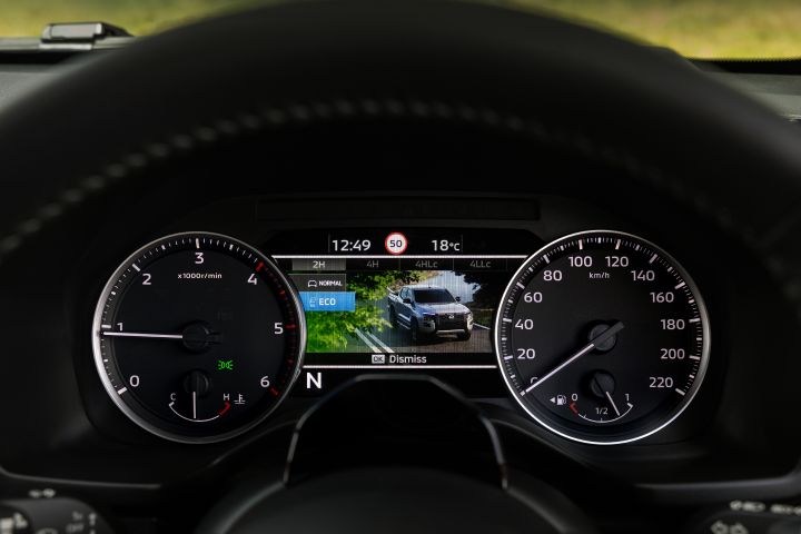 2026 Nissan Navara PRO-4X finished in Boulder Grey shown in a front three-quarter driving shot with black wheels, side steps and red-highlighted grille trim.