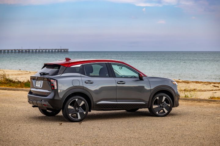Right rear 3/4 view of a silver 2025 Nissan Kicks parked on a gravel lot overlooking a beach and Pier.
