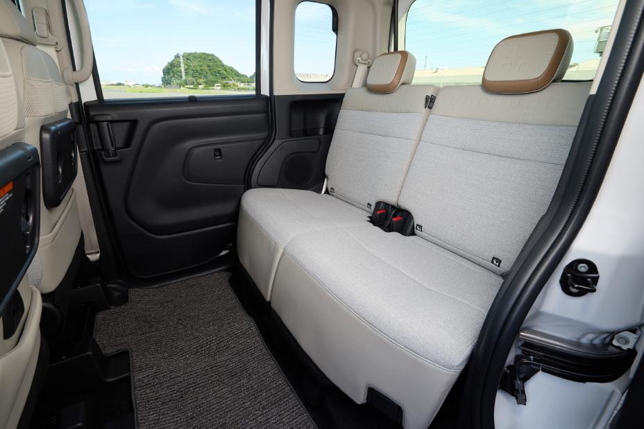 Rear seats of the new Nissan Roox kei car. The greige seats have two headrests, with a door and window visible. A green landscape can be seen outside the window.