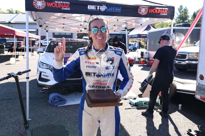 Nissan Sentra Cup driver, Valerie Limoges, in her racing suit, presenting her trophie while holding up one finger and smiling