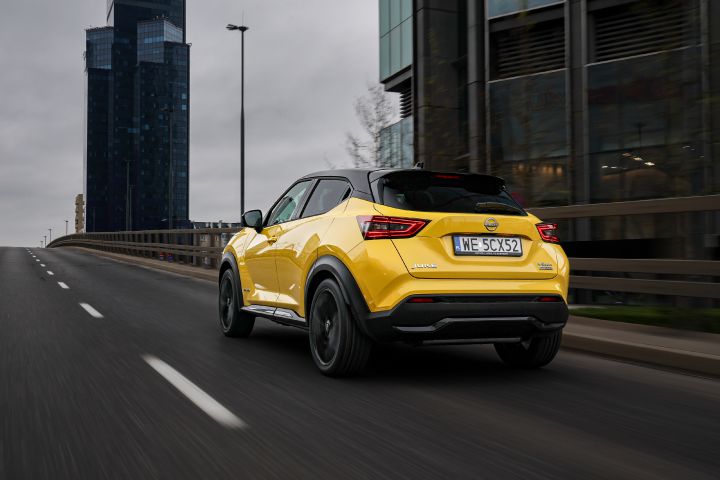 Jadący żółty Nissan Juke (widok z tyłu) z budynkami w tle