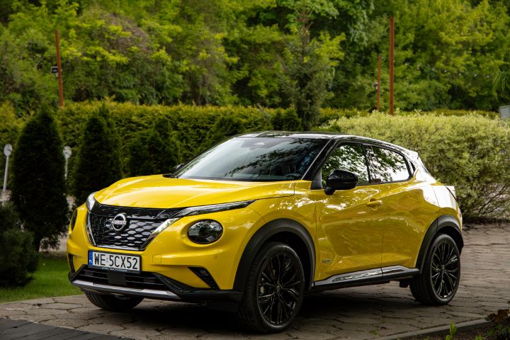 Stojący żółty Nissan Juke (widok z boku) na tle zieleni