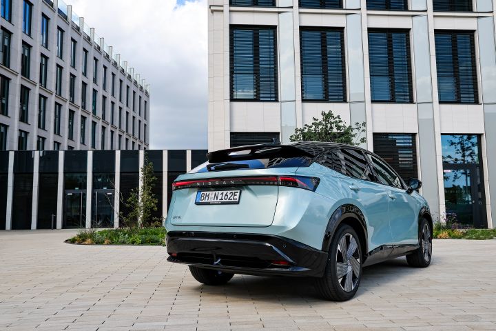 Blick von unten und schräg hinten auf einen hellblauen Nissan Ariya, der auf einem hell gepflasterten Platz steht