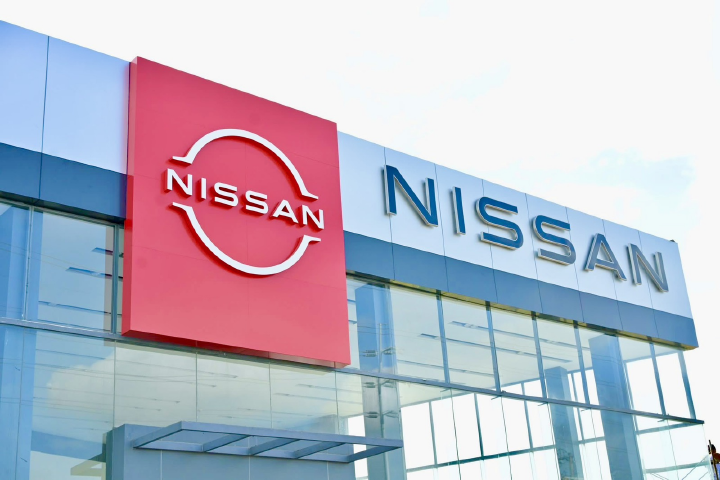 Nissan dealership exterior with a modern glass façade, featuring a red Nissan logo panel on the left and large silver “NISSAN” lettering across the building