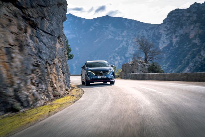 Photo de l’avant de l’Ariya Nismo roulant dans un virage  aux pieds de la montagne.