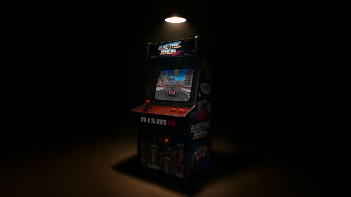Old arcade game machine on a dark background with NISMO branding on it, with the screen illuminated showing the NISMO Electric Racer game logo and a Nissan FE car on the screen.