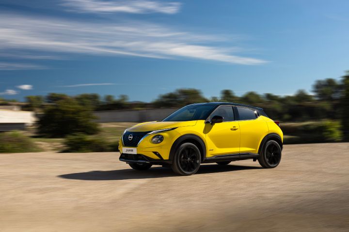 Gele Nissan Juke rijdend over de weg onder een blauwe lucht en met groene bomen op de achtergrond.