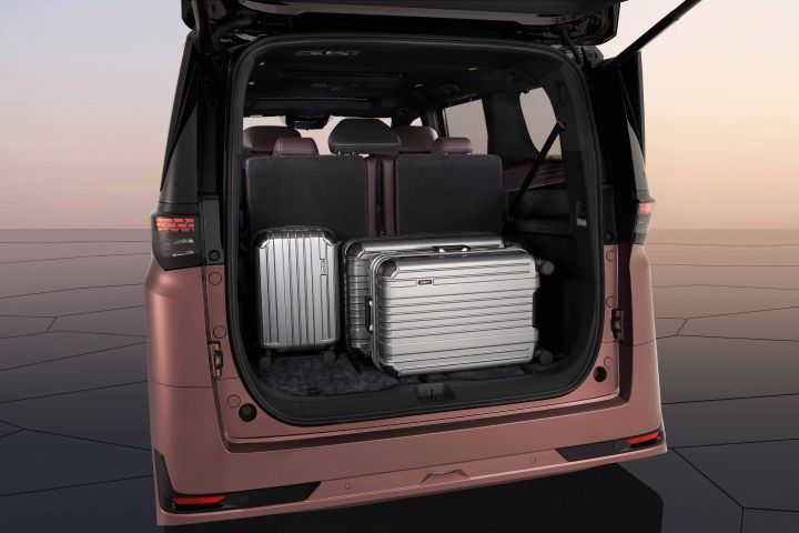 The trunk of a Fuji-dawn-colored Elgrand is open, with two suitcases stored inside.