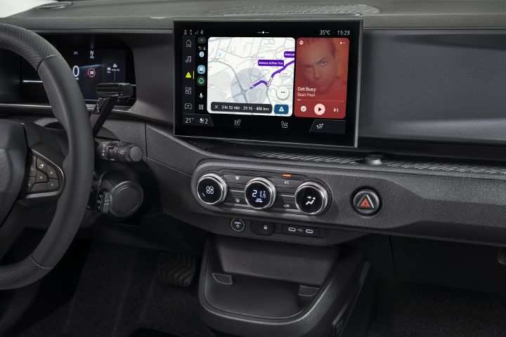 Photograph of a modern vehicle dashboard showing Waze and Spotify screens, steering wheel, climate controls, hazard button, and storage compartment.