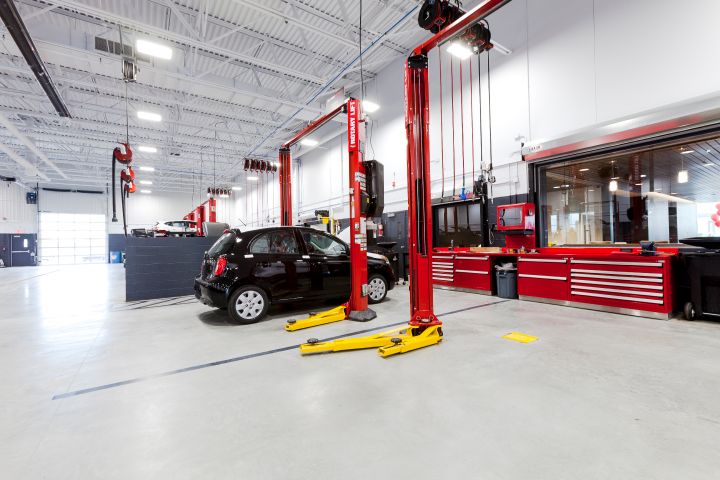 Un atelier de réparation de véhicules spacieux et bien éclairé avec des outils et une voiture noire soulevée par un ascenseur hydraulique rouge.