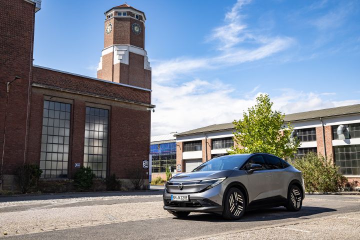 Ein grauer Nissan Leaf steht auf einem Platz vor älteren Industriegebäuden und einem hohen gemauerten Turm