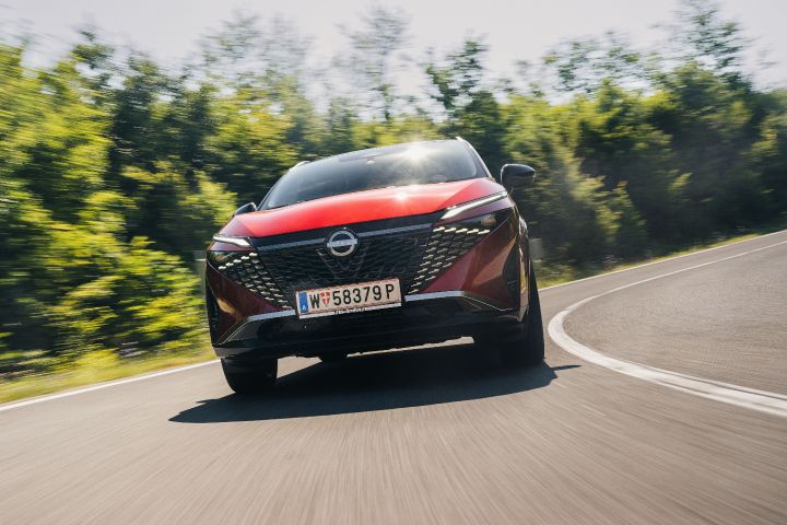 Dynamische Frontansicht auf einen Nissan Qashqai in Fuji Sunset Red, der auf einer Landstraße durch eine Kurve färt