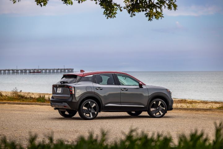 Tilted right profile view of a silver 2025 Nissan Kicks parked on a gravel lot overlooking a beach and Pier.