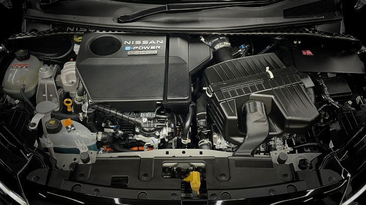 Full view of the NISSAN e‑POWER VC TURBO engine bay. The center features a black engine cover with the text 'NISSAN', 'e‑POWER', and 'VC TURBO'. On the right side is a large air cleaner box, while the left side shows coolant reservoirs and oil caps among other auxiliary components. The overall design is predominantly black with metallic parts and hoses, highlighting the intricate mechanical structure.