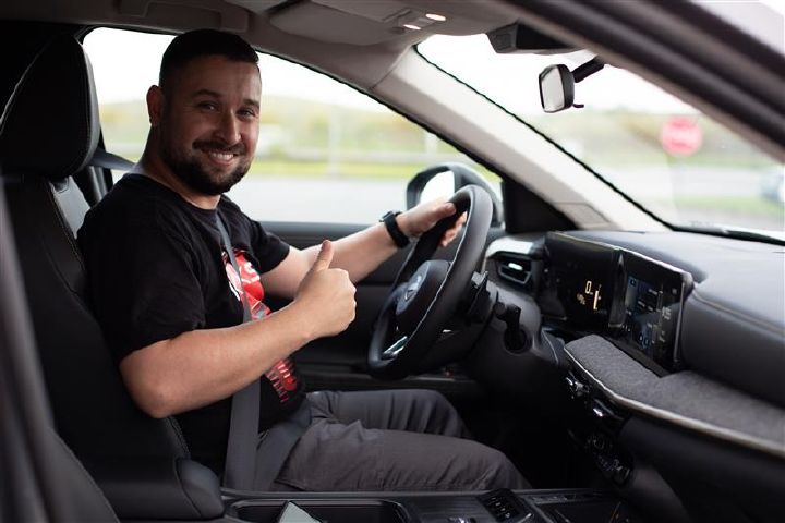 Homem sentado ao volante de um carro Nissan, sorrindo e fazendo sinal de positivo com a mão