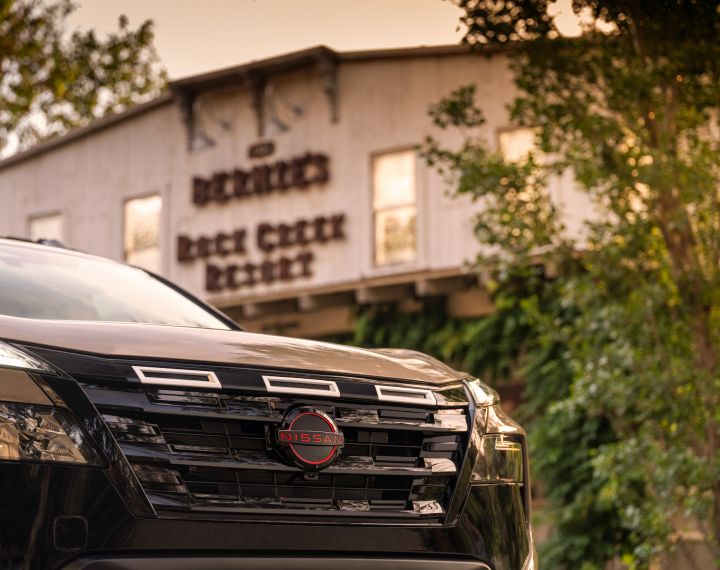 Close up of the grill on a 2025 Nissan Rogue rock creek, "Rock creek resort" building and sign is in the background.