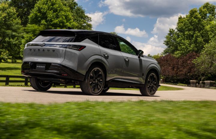 Rear angled view of the 2027 Nissan Murano Dark Armor parked on a residential road with a fence and trees behind.