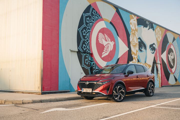 Ein Nissan Qashqai in Fuji Sunset Red steht vor einer Wand mit einem bunten Grafitti-Kunstwerk