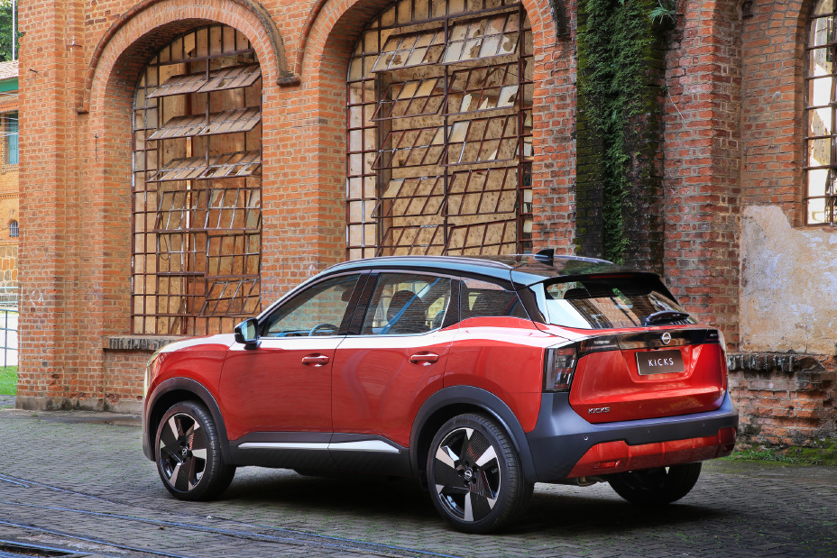 Novo Nissan Kicks Platinum na cor vermelha visto de traseira. Atrás, uma parede feita de tijolos
