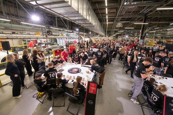 Wide photo with Nissan Lego Qashqai being built by kids with Nissan manufacturing production line in the background